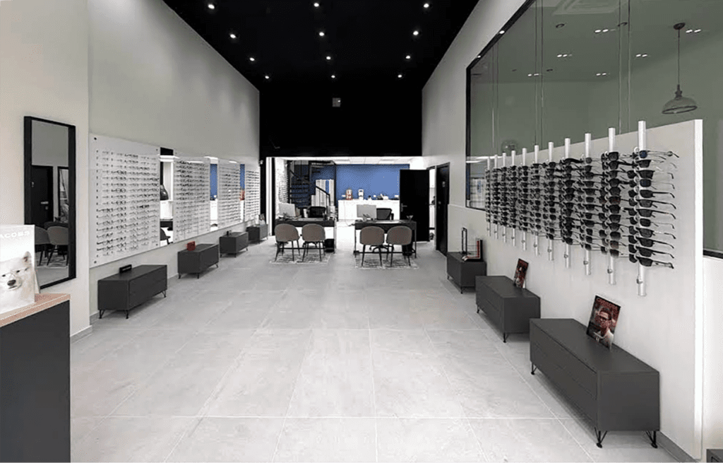 Vue d’ensemble d’un magasin d’optique moderne avec présentoirs muraux de lunettes, circulation fluide et espace d’accueil lumineux et épuré.