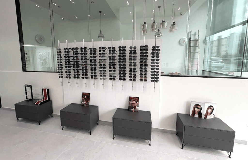 Mobilier d’agencement pour opticien avec présentoir de lunettes solaires sur panneaux muraux et rangements bas design en finition gris mat.
