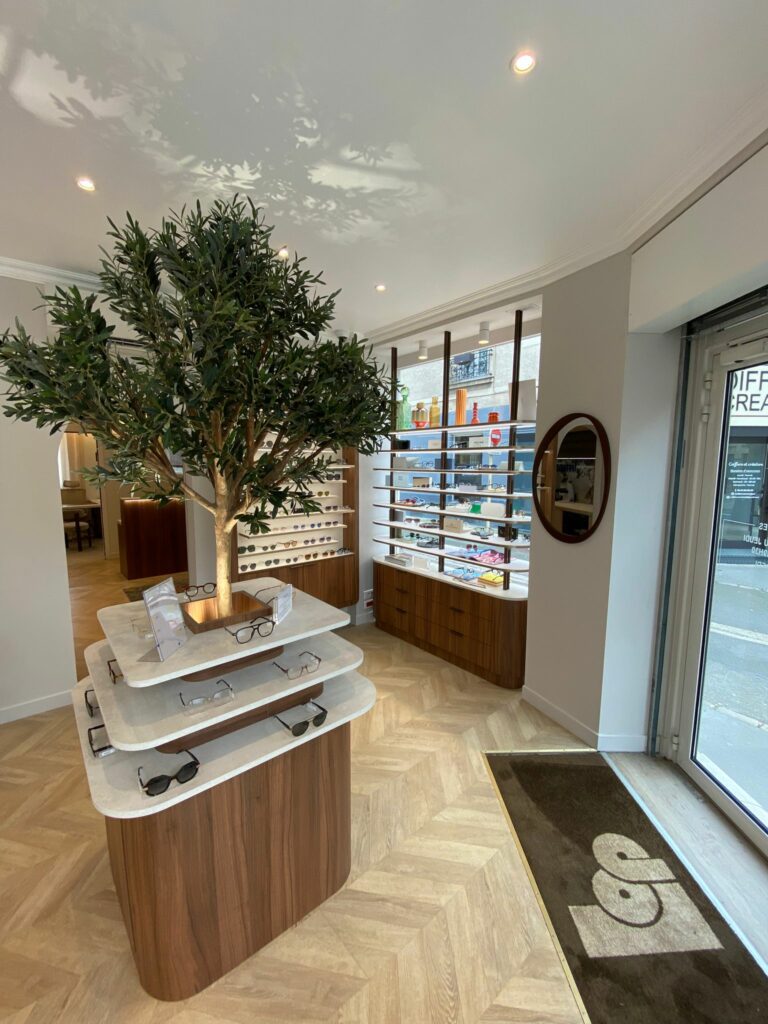 Espace bureau pour opticien avec mobilier bois et blanc, fauteuils confortables et éclairage doux pour l’accueil et le conseil client.