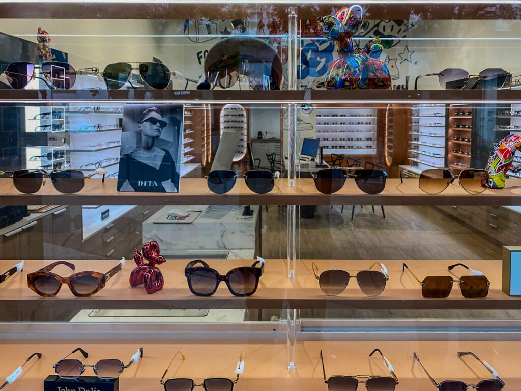 Vitrine de magasin d’optique avec présentation de lunettes solaires sur étagères en bois et mise en scène élégante des produits.