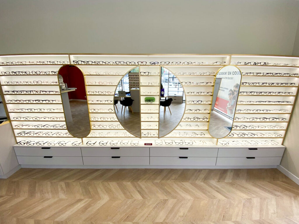 Grand mur de présentation rétroéclairé avec miroirs intégrés et rangement pour lunettes dans un magasin d’optique