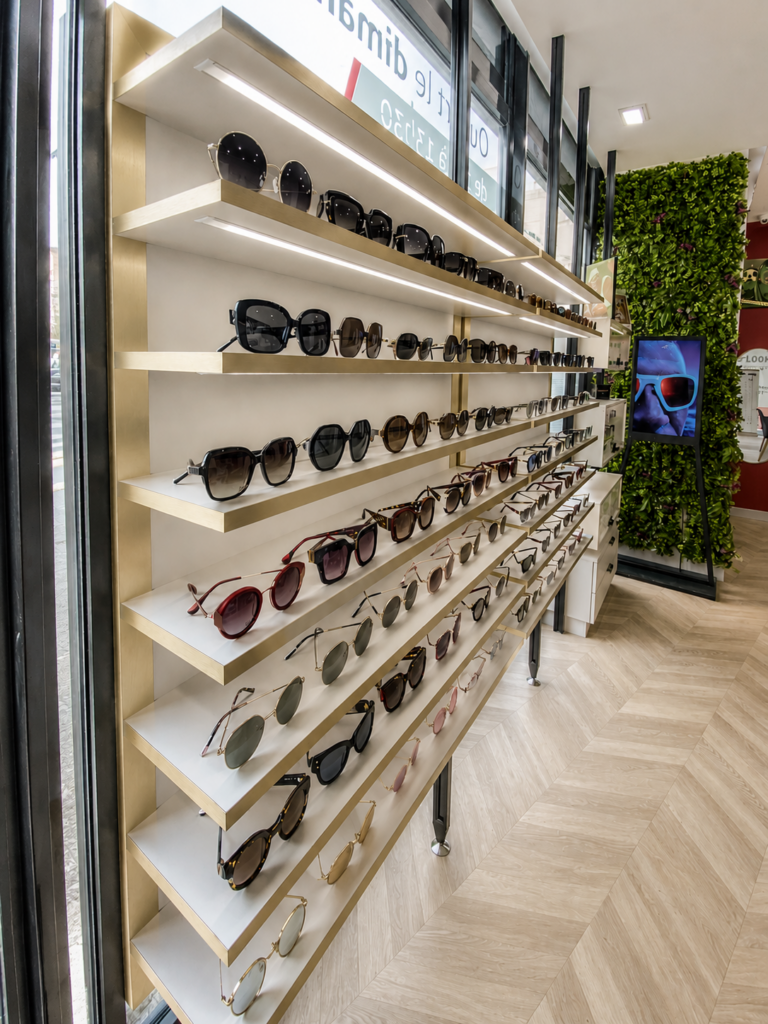 Présentation de lunettes solaires sur mobilier rétroéclairé avec finitions dorées dans un magasin d’optique moderne